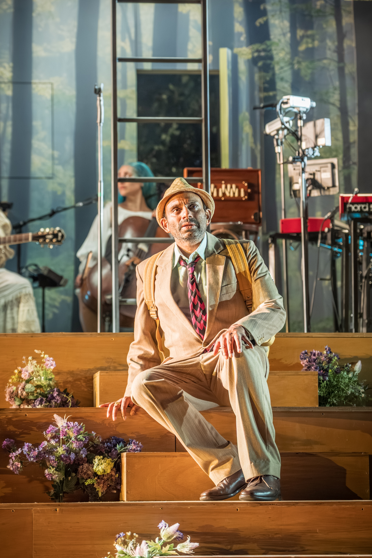 Egeus (played by Neil D’Souza) sits despondently on a set of stairs. This is a production of “A Midsummer Night’s Dream” performed at Regent’s Park Open Air Theatre (London) in 2026. Photography by Marc Brenner.