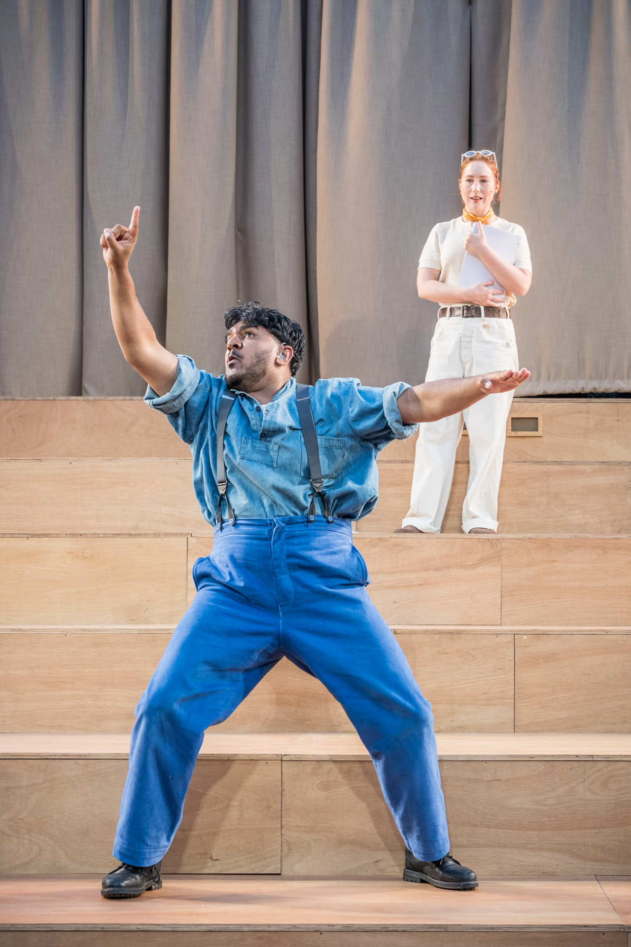 A man in blue has his arms in the air as he is mid-gesticulation. The man is Bottom (played by Nadeem Islam). This is a production of “A Midsummer Night’s Dream” performed at Regent’s Park Open Air Theatre (London) in 2026. Photography by Marc Brenner.